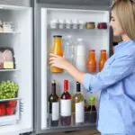 a female wearing blue shirt is putting a bottle of juice in the fridge